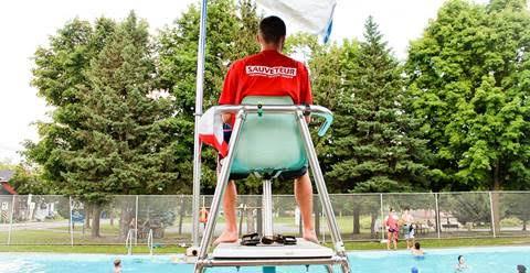 A lifeguard watching over the swim zone from an elevated wooden watchtower on a sunny beach.