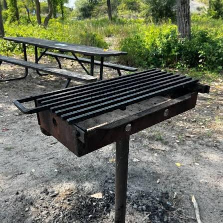A beachside BBQ station with a charcoal grill, grilling tools and fresh seafood ready to cook.
