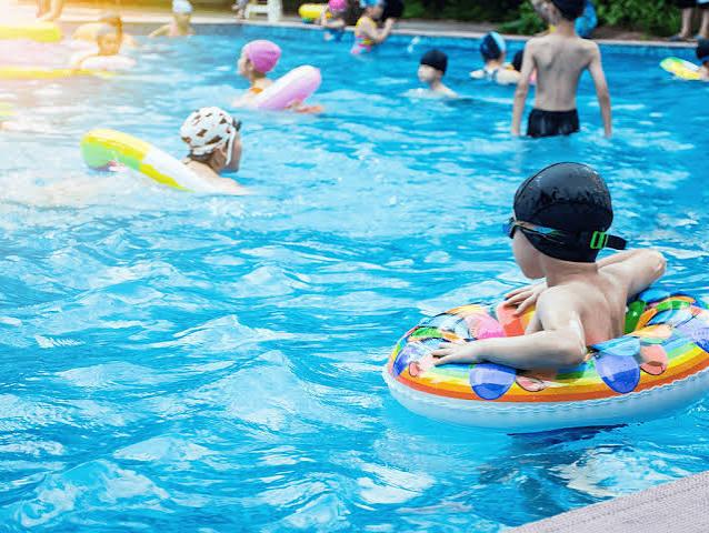 A colorful shallow children's pool with water jets and a small slide, kids playing under the sun.