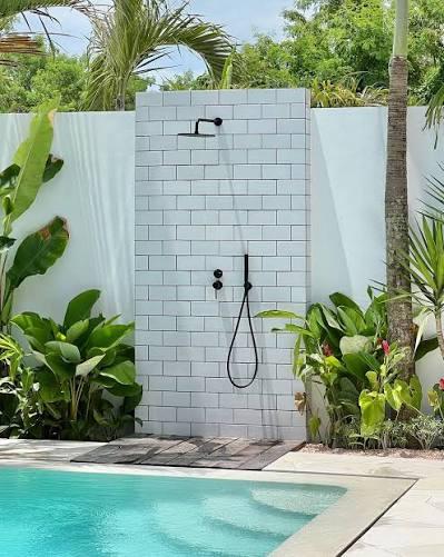 An open-air beachside shower station with wooden panels surrounded by tropical plants.